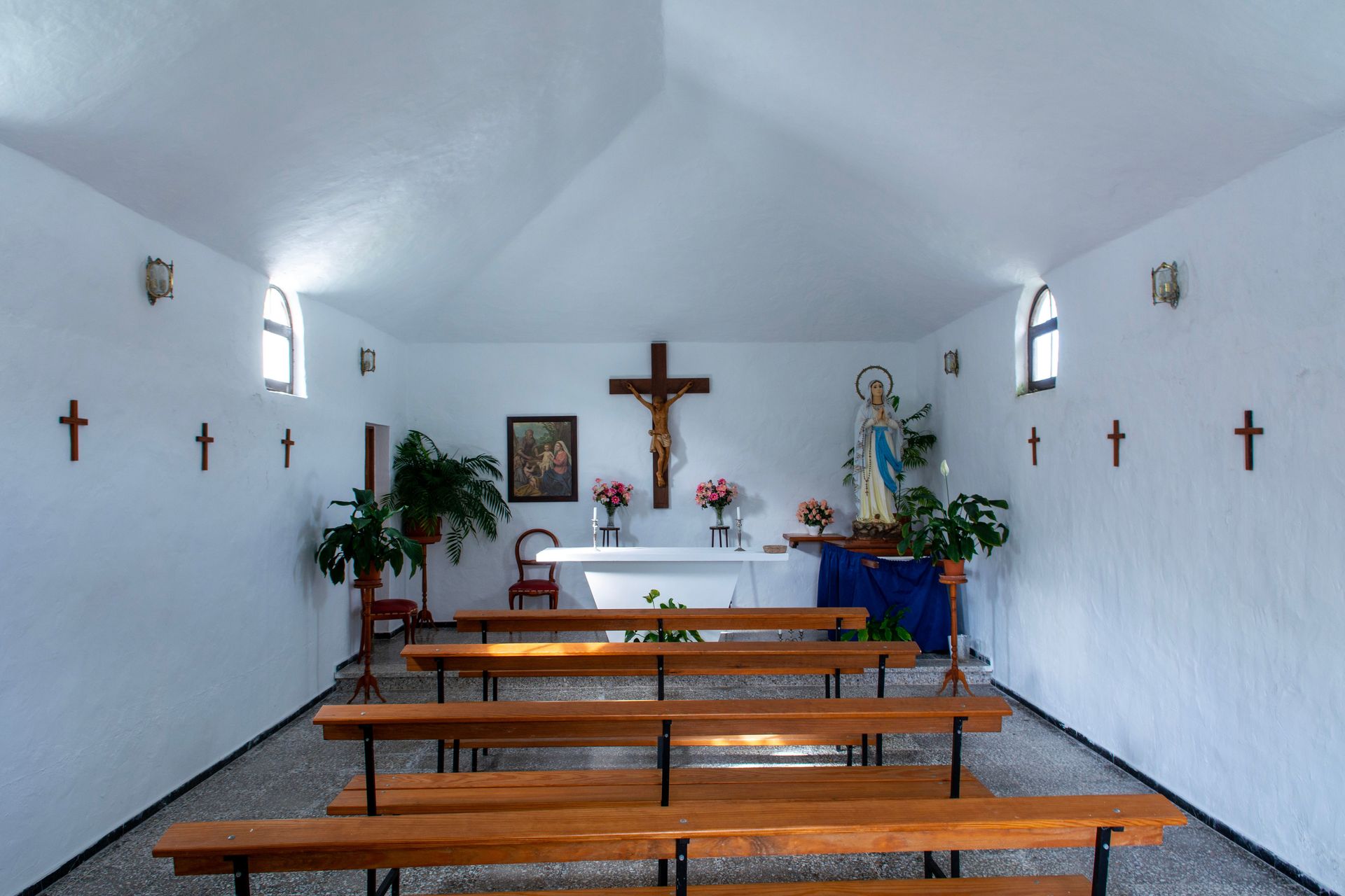 Peaceful interior of a chapel in Guinate, Spain, featuring benches, crosses, and an altar.