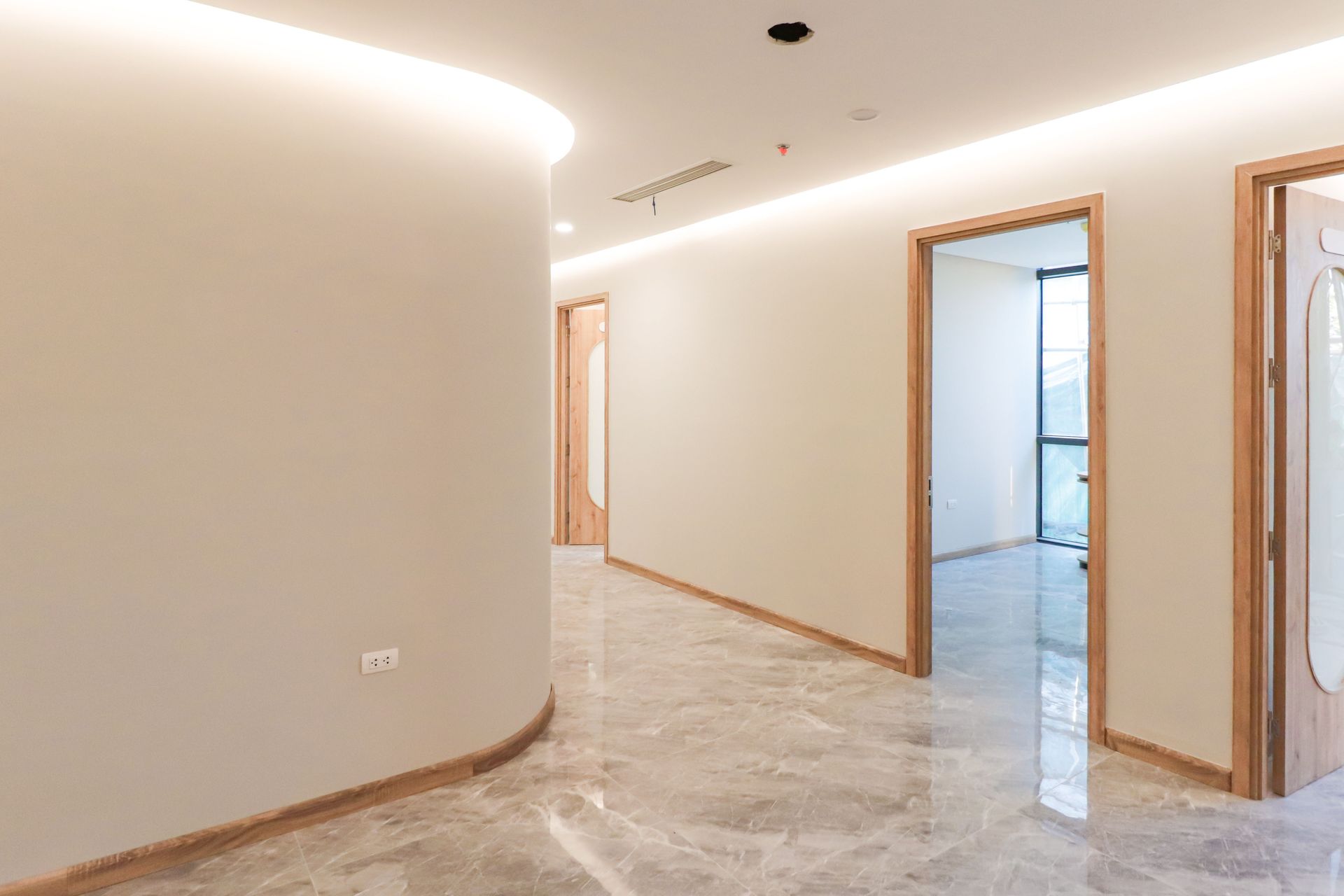 Bright, minimalist corridor with marble flooring and wooden door frames in a modern office setting.