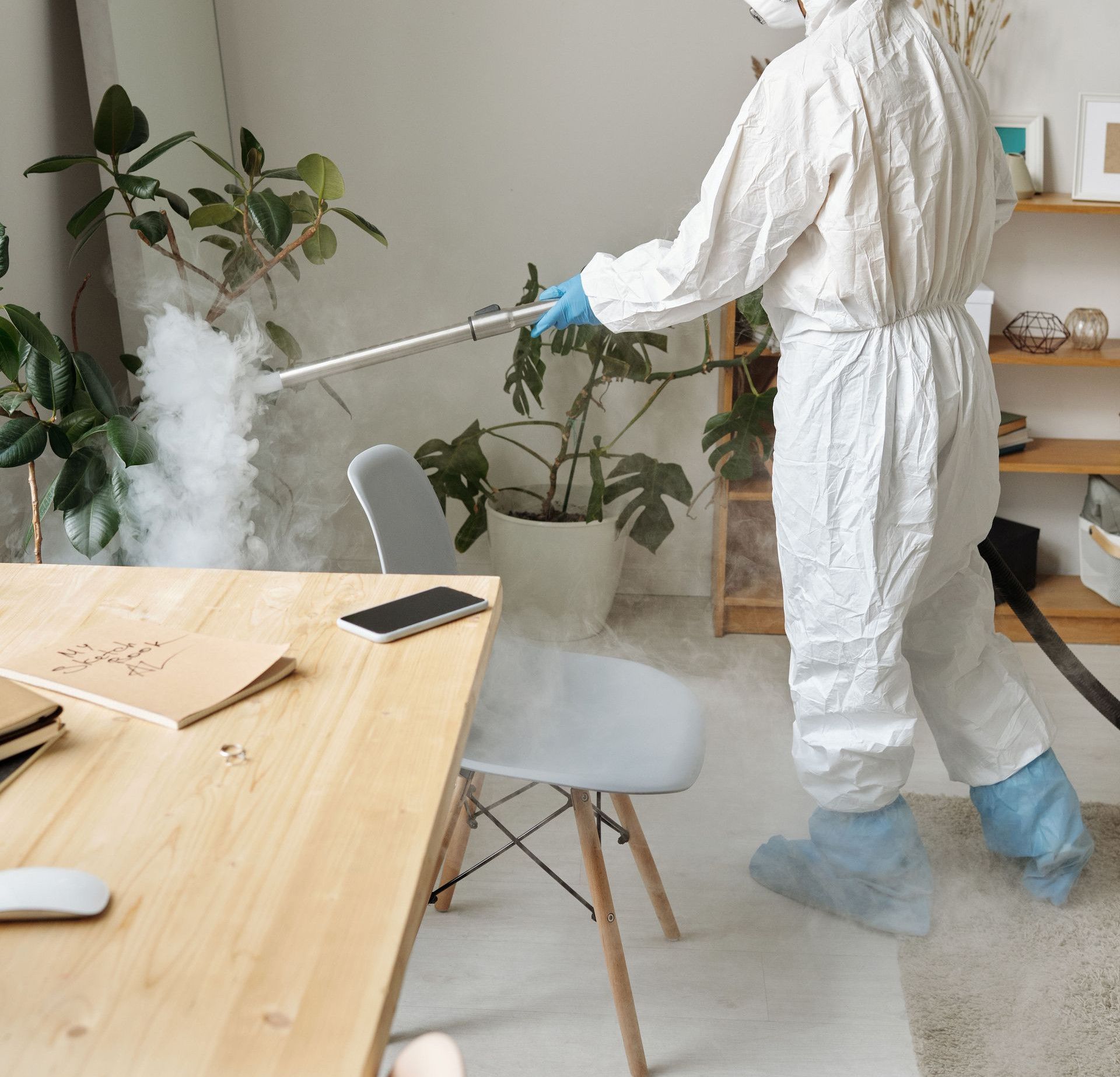 Person in protective suit disinfecting office for virus control.